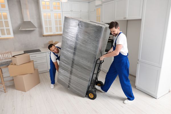 Two appliance technicians shipping a refrigerator into a kitchen 