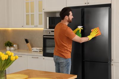 A man cleaning a black stainless steel refrigerator 