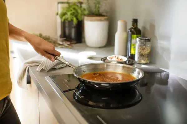A person preparing a meal on the Electrolux ECCI3068AS induction cooktop