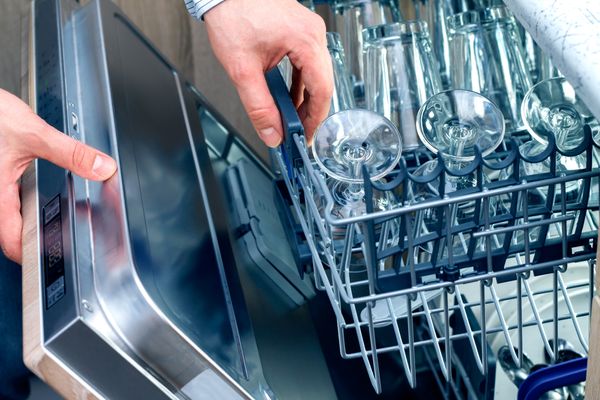A person reaching into a dishwasher full of glassware 
