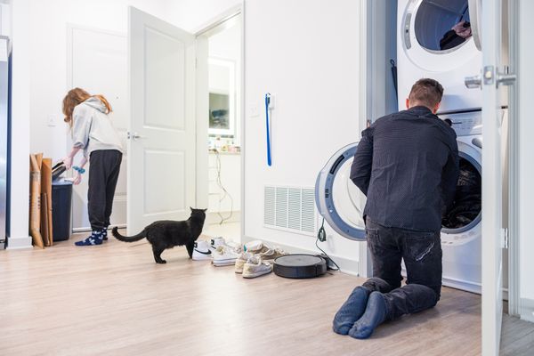 A man unloading a washer while a cat and woman are in the background 