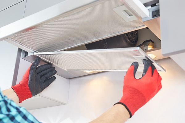 A person wearing red gloves changing a filter on a range hood 