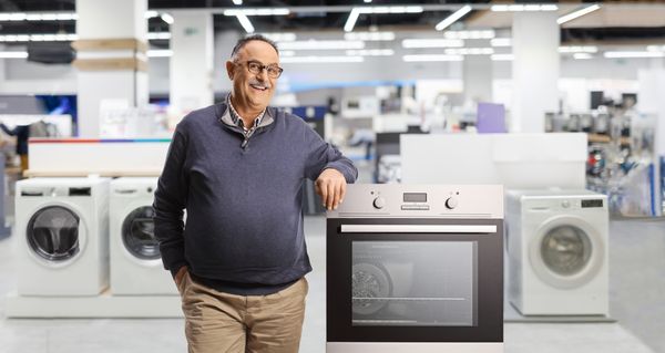 A senior appliance shopper smiling next to an oven with appliances in the background 