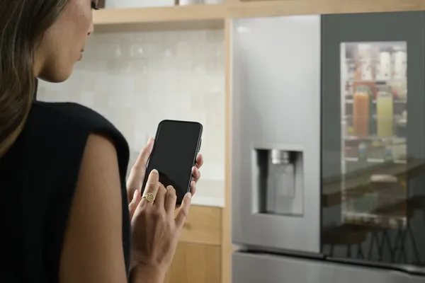 A woman using a smart device paired to the LG LRYKC2606S smart refrigerator