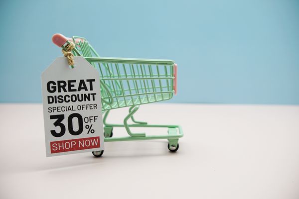A miniature green shopping cart with a sale tag against a blue background 