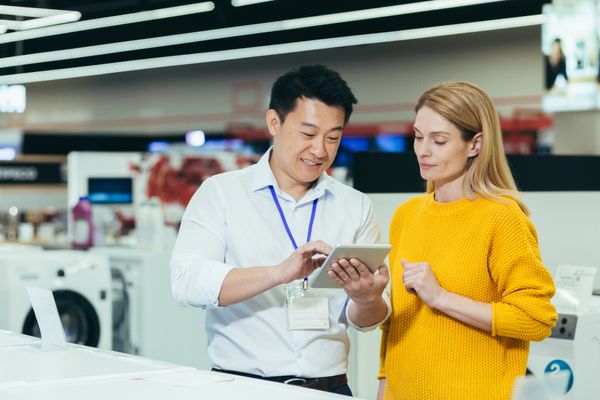 A salesman showing a woman in a yellow sweater something on a tablet 