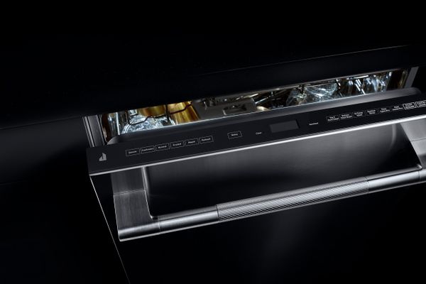 An editorial shot of a JennAir dishwasher with its door open against a black background 