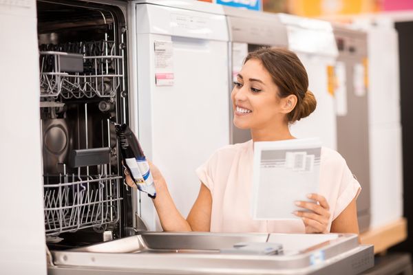 A woman smiling while reviewing a dishwasher in a store 