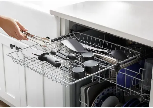 A user placing tongs inside the GE GDT630PYRFS dishwasher third rack 