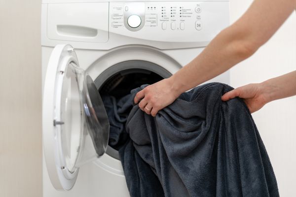 A person putting a black throw blanket in a washer
