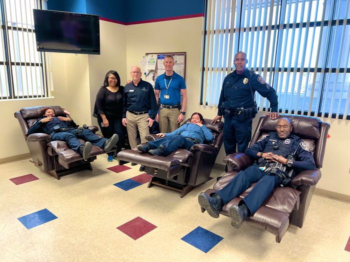 BlvdHome and North Las Vegas Police Department staff gather for a donation presentation as NLVPD officers enjoy relaxing in La-Z-Boy recliners.