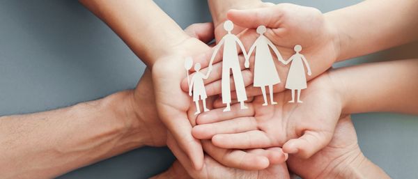 Multiple hands join to hold paper cut into the shape of a family
