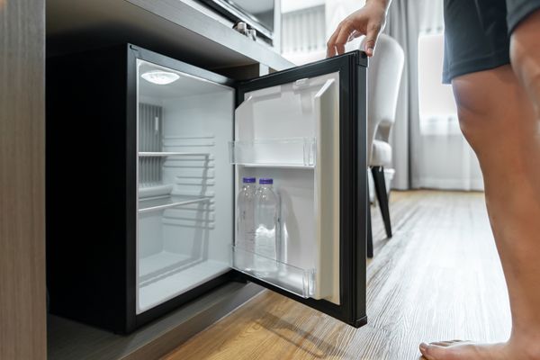 A close-up of a person standing next to a mini refrigerator 