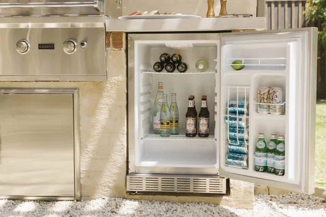 Front view of an opened outdoor refrigerator in a modern outdoor kitchen with a Coyote grill.