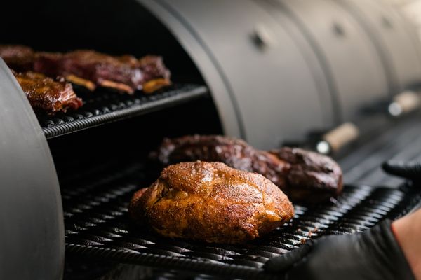 A close-up look of a person removing a grilled chicken from a grill 