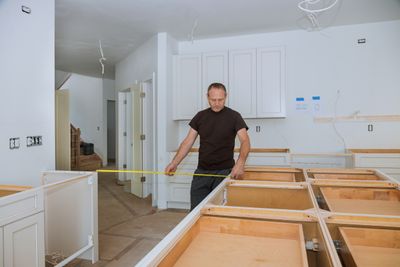 A man measuring the distance between two kitchen cabinets 