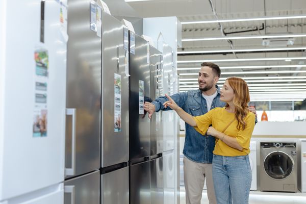 A man and a woman smiling while reviewing refrigerators in a store 
