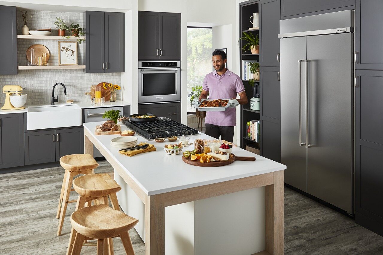 A man in a purple polo holding a casserole dish next to a KitchenAid KBSD702MPS refrigerator 