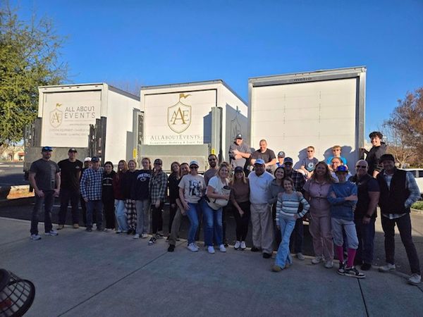 SLO Community volunteers stand in a group in front of 3 delivery trucks