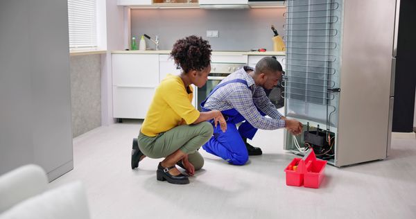 A woman overlooking a repair technician fixing a refrigerator