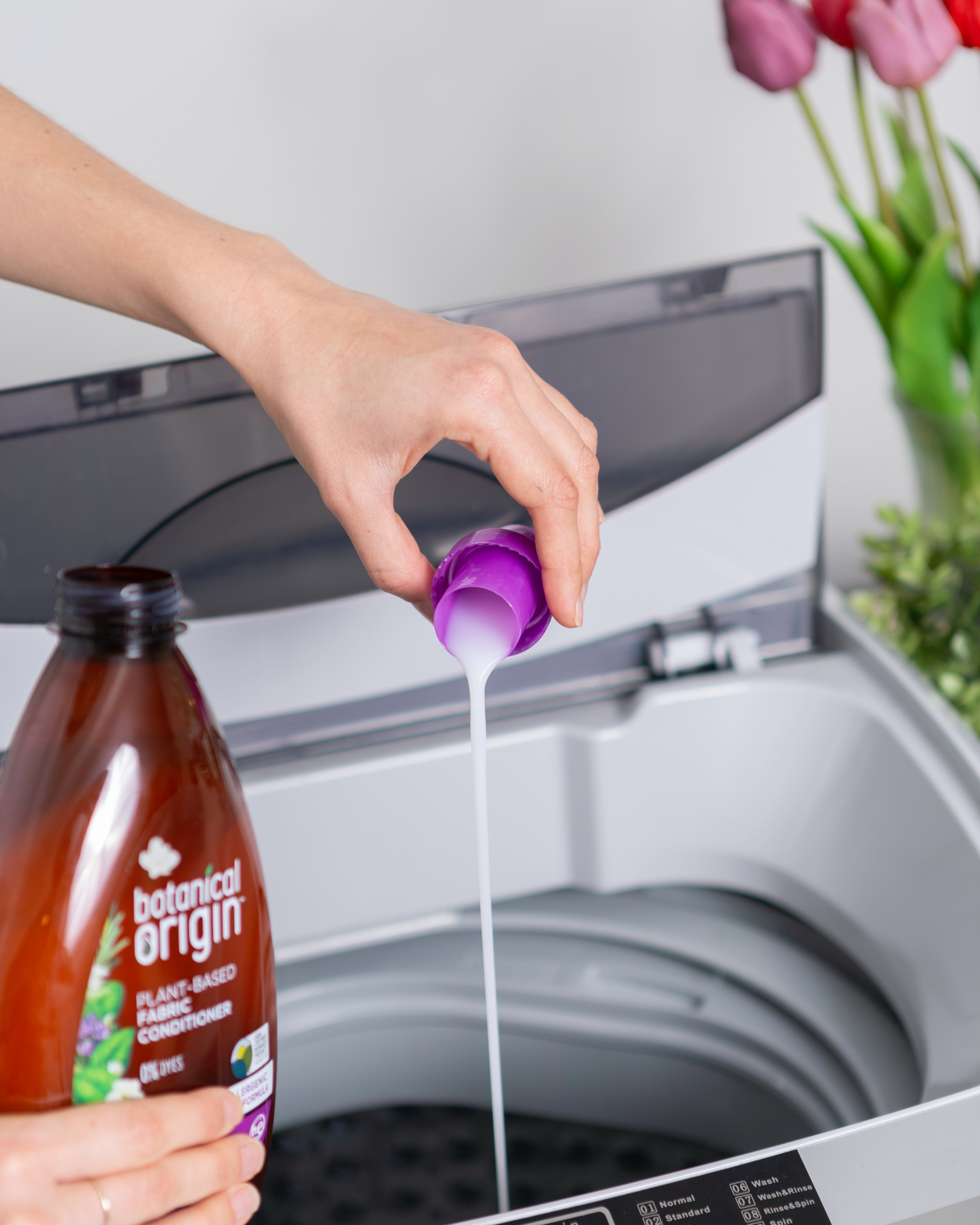 A woman pours cleaning solution into a top load washing machine