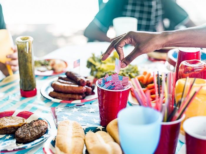 Picnic table with Fourth of July themed decoration and various barbeque food items.