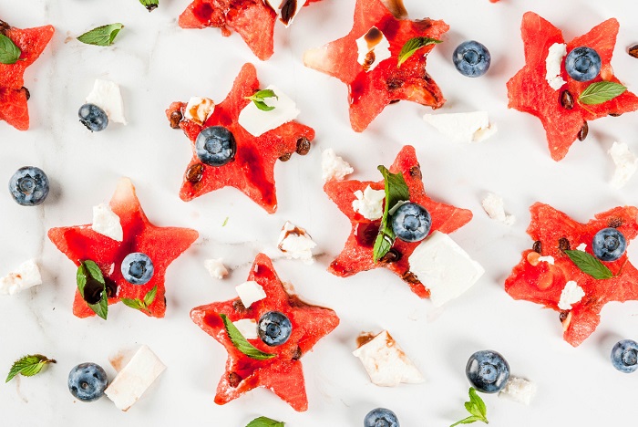 Watermelon sliced in the form of stars, blueberries, feta cheese and balsamic sauce on a white marble table.