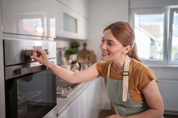 A smiling woman adjusting an oven setting