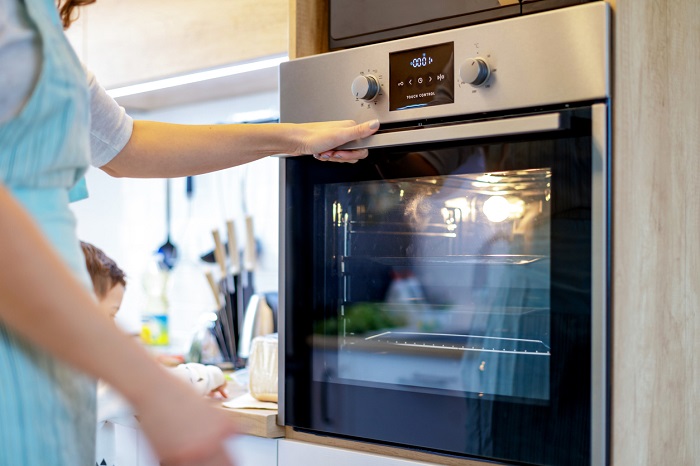woman in apron checking baked goods in wall oven