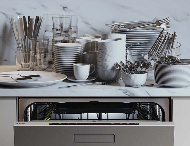 Front view of an ASKO dishwasher with 16 place settings worth of dishes on the counter above