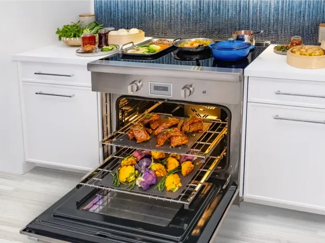 Credit: BSH Group, Thermador | Front view of a Thermador induction range with various pans and foods cooking on top. The oven is open with various pans of food cooking inside.