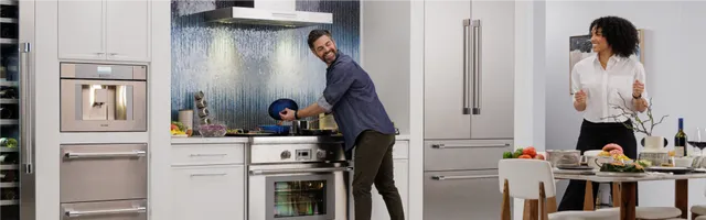 Credit: BSH Group, Thermador | Wide angle view of a modern kitchen with Thermador appliances and a man smiling and cooking on a Thermador induction range