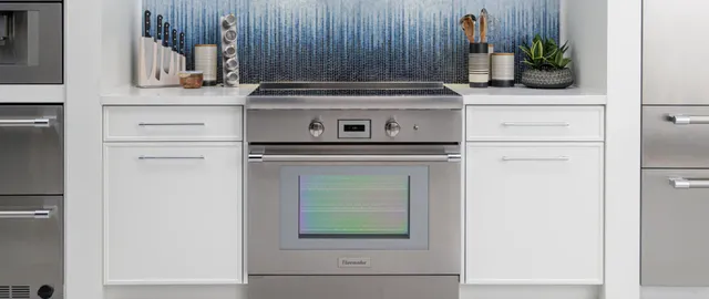 Credit: BSH Group, Thermador | Front view of a Thermador induction range in a modern kitchen with white cabinetry and a blue backsplash.