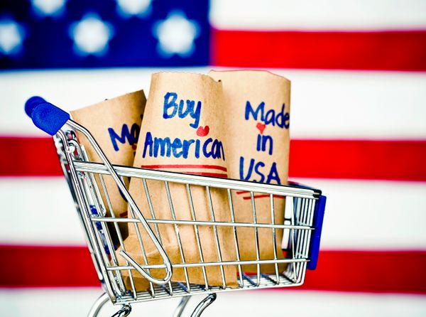 A mini shopping cart with paper bags with Buy American and Made in USA written on them 