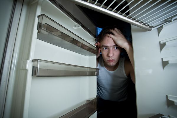 A concerned man looking into a refrigerator 
