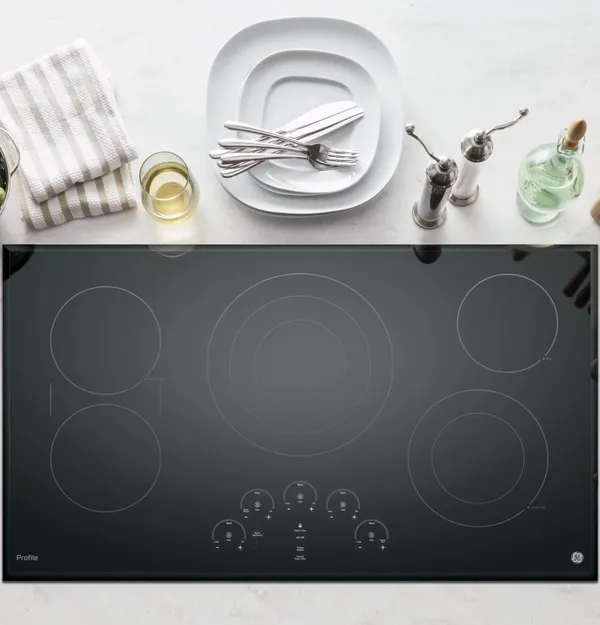 GE Profile electric cooktop surrounded by various cooking utensils and tools