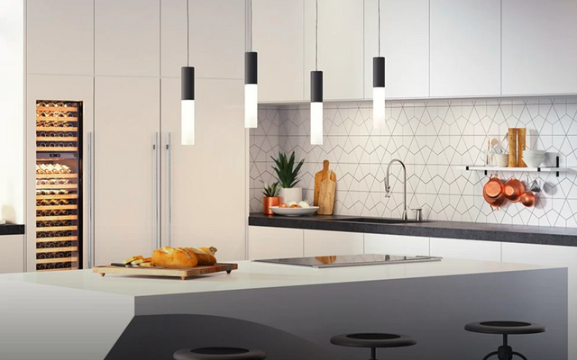 front view of a modern ktichen with white cabinets and a grey island with a Wolf induction cooktop built in and bread on a serving board beside it