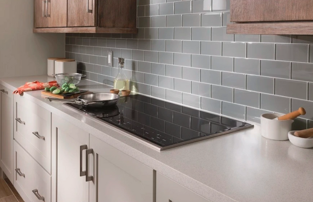 standing view of a modern kitchen with white cabients, white countertops, and a black wolf induction cooktop with various cooking ingredients around it