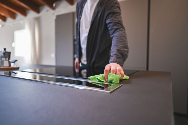 View of a man using a green cloth to wipe down an induction cooktop 