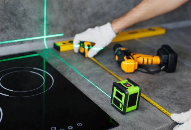close view of a person measuring the edge of a cooktop in a countertop with a level light and measuring tape