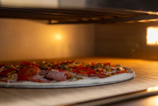 Close view of a thin crust pizza cooking inside a stainless steel electric pizza oven.