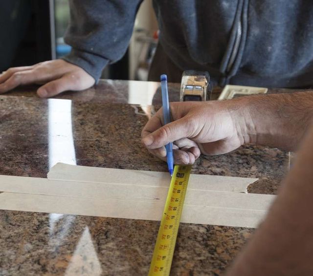 close view of two mens hands taping and measuring a marble island countertop 