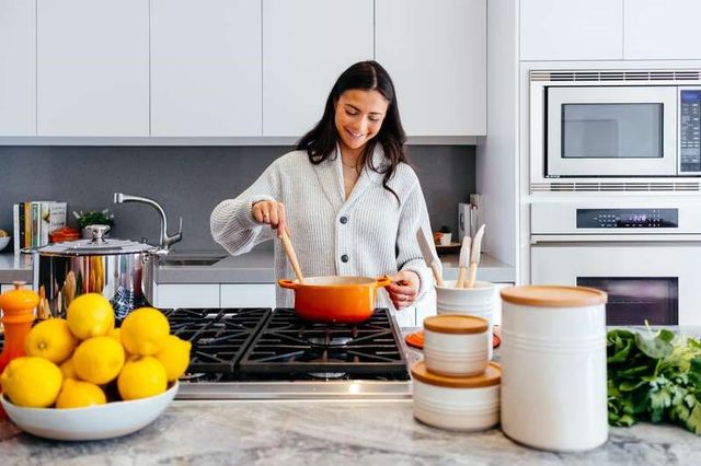 front view of a woman cooking on her kitchen island range in a modern white kitchen