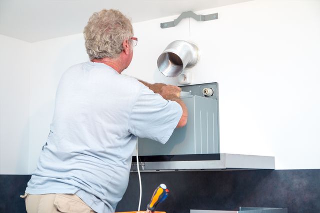 View of a man installing a ducted kitchen range hood