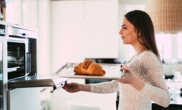 side view of a woman using her steam oven reheat a croissant on a pan