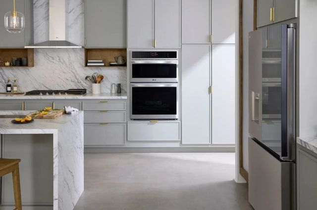 front view of a wall oven and microwave combo in a modern kitchen with white cabinets and marble counters and backsplash