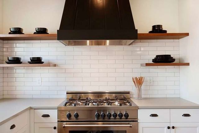 front view of the top of a range and a range hood in a modern kitchen with a white backsplash and wall