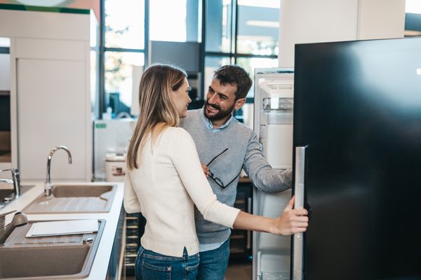 A man and a woman smiling while reviewing a refrigerator 