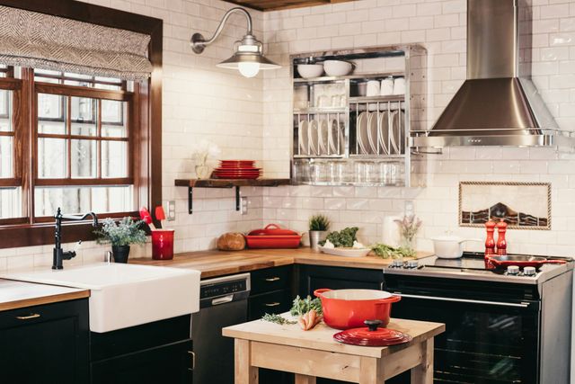front view of a modern kitchen with white subway tile walls, black cabinets, black applianes, and a stainless steel wall mount range hood