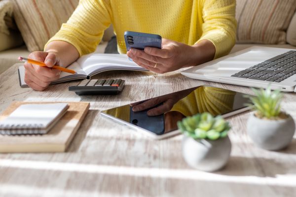 A person in a yellow shirt crunching numbers on a phone and calculator 